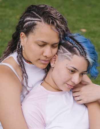 Two people sit on the grass arm in arm.