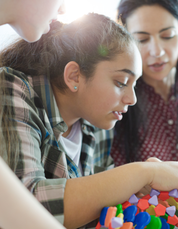 A high school student engages in a hands-on project while a teacher and fellow student look on.