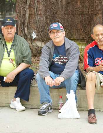 Three older men sitting on a wall.