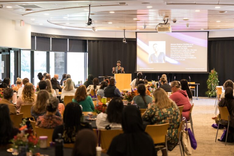 A conference room with a female speaker addressing a full room of attendees.