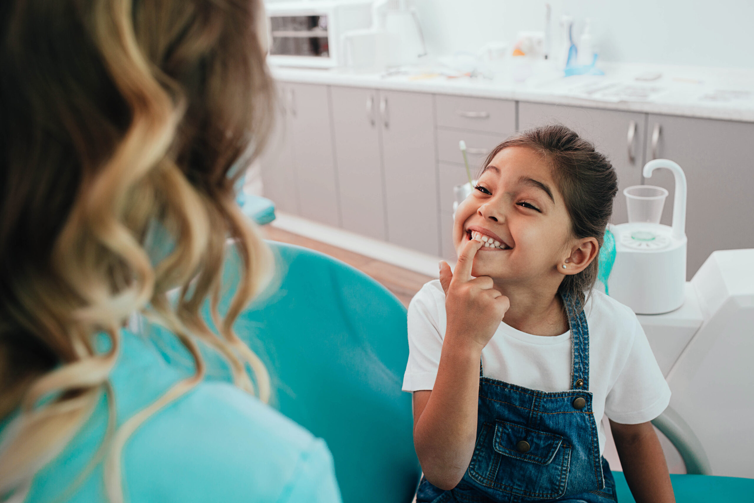 Mixed race little patient showing her perfect toothy smile while sitting dentists chair