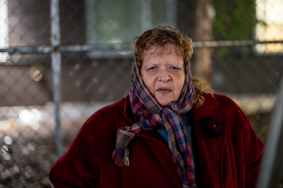 A woman in a thick coat and headscarf looks into the camera