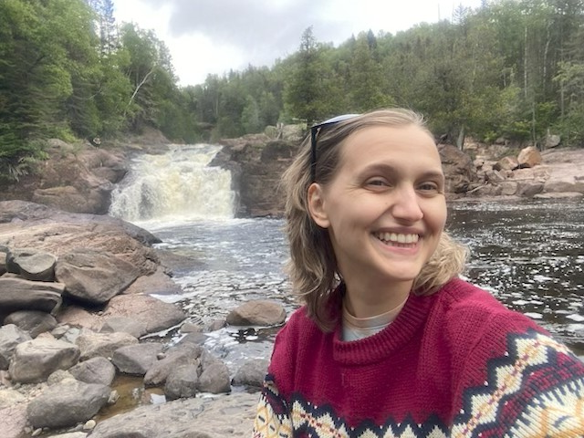 A person smiling in front of a waterfall and river