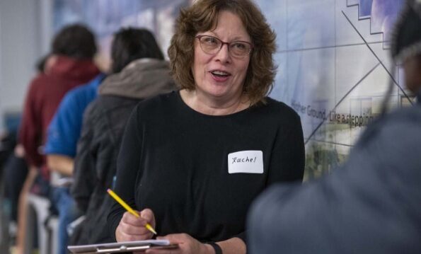 Photo of a woman sitting with a pencil and clipboard as she interviews a person.