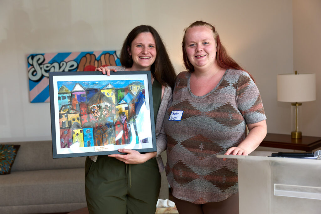 Two women standing next to each other with one holding a colorful painting