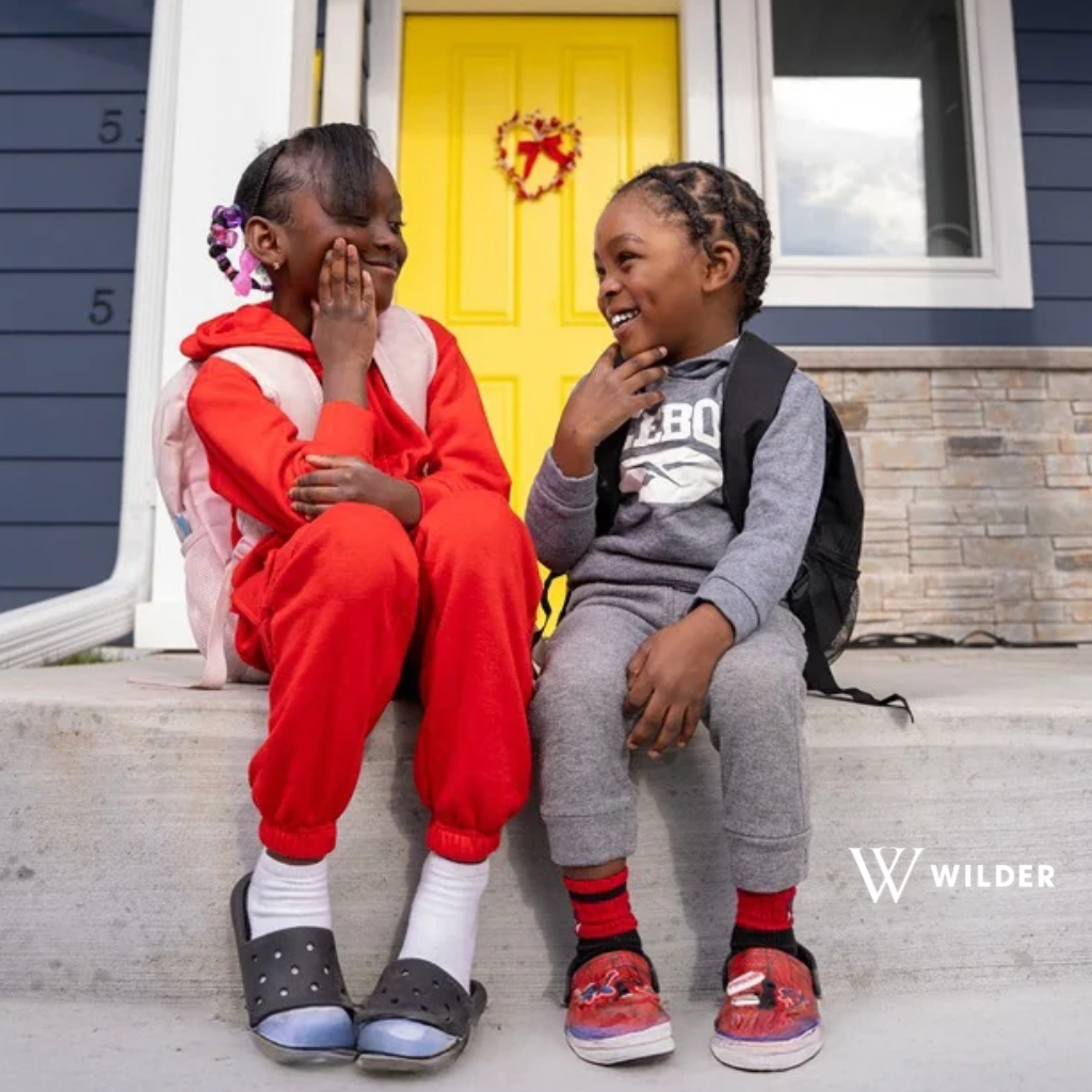 Photo of two children sitting on the stoop of a house as they look at each other with smiles.